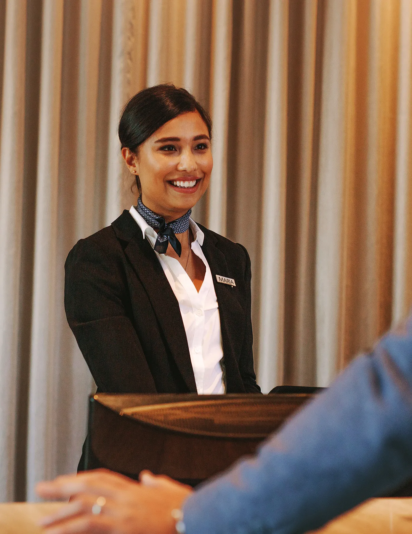 Smiling event hostess standing at a check-in podium while greeting a guest at an indoor reception