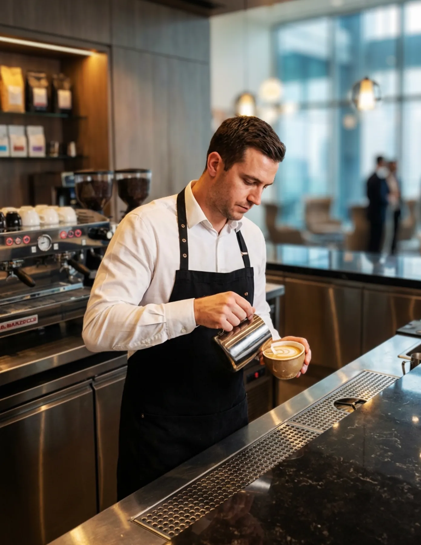 Barista wearing an apron pouring steamed milk to create latte art behind a modern café counter