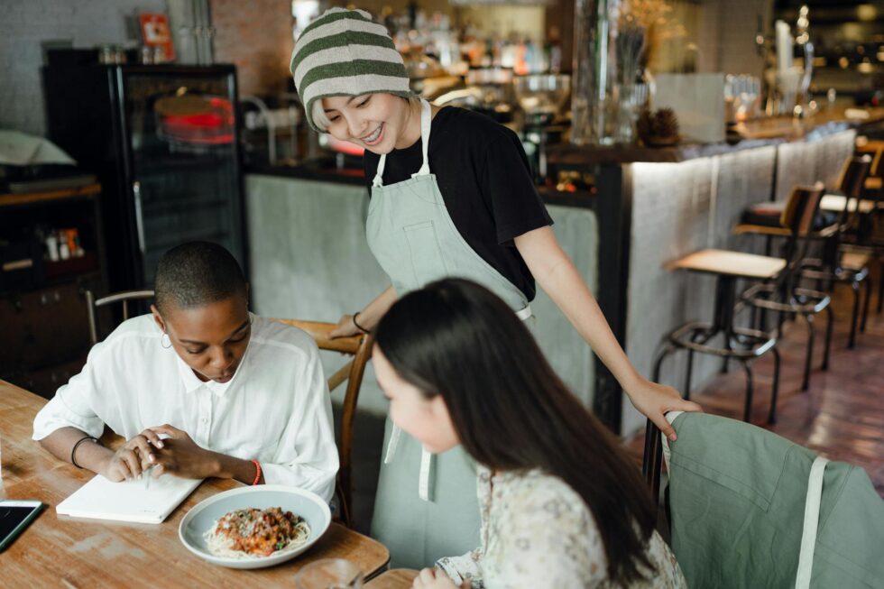 Smiling restaurant server in apron attentively engaging with guests at a casual dining venue staffed by HMG+ hospitality professionals