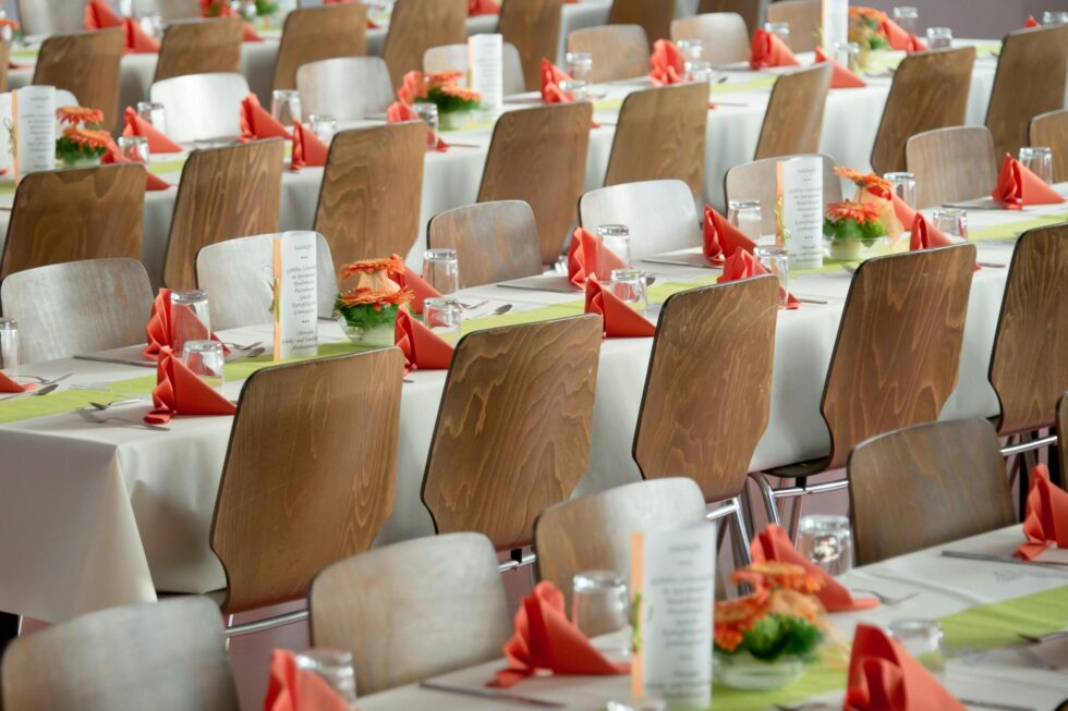 Rows of elegantly set banquet tables with orange linen napkins and floral centerpieces ready for a large corporate dinner or gala event