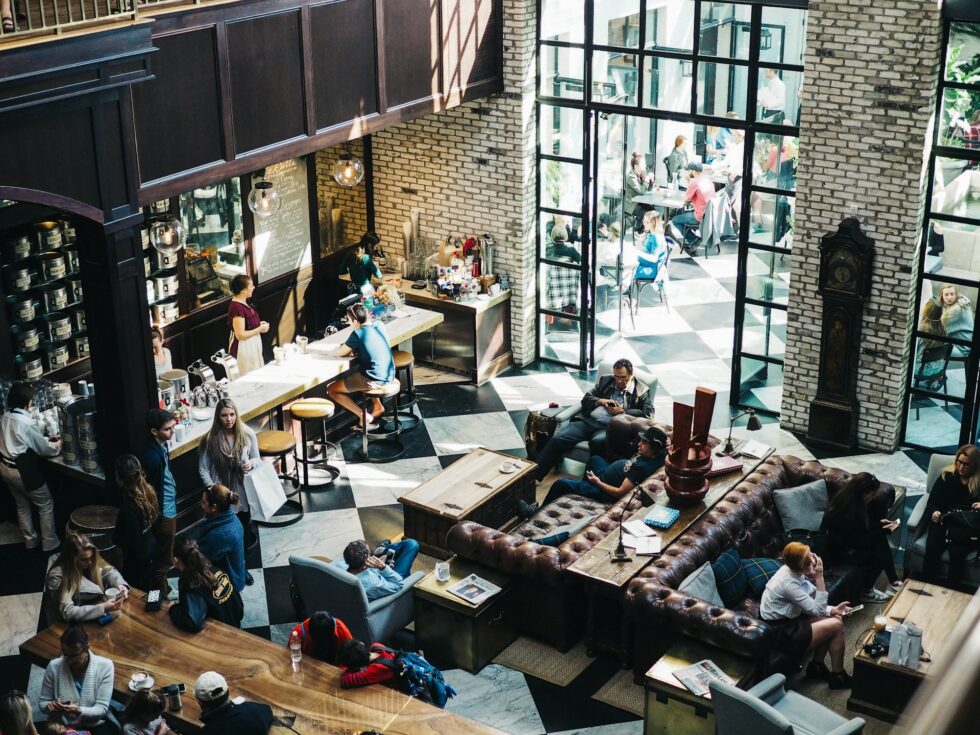 Guests and staff filling a grand luxury hotel lobby with high ceilings, designer furnishings, and a bustling bar area in New York
