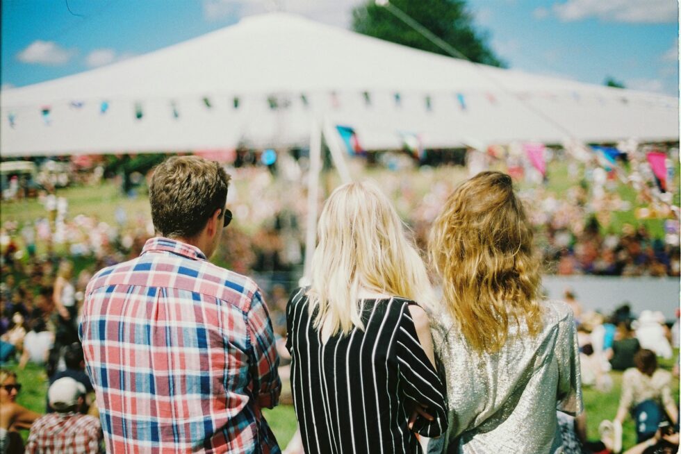 Guests gathered at a large outdoor concert festival with a white event tent and crowd of attendees on a sunny day