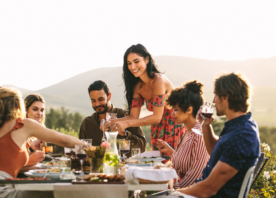 Guests enjoying an outdoor dinner while a hostess pours wine at a catered event.