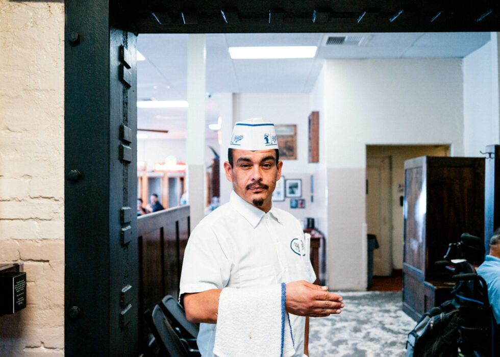 Professional catering staff member in uniform greeting guests at the entrance of an upscale restaurant or private event venue