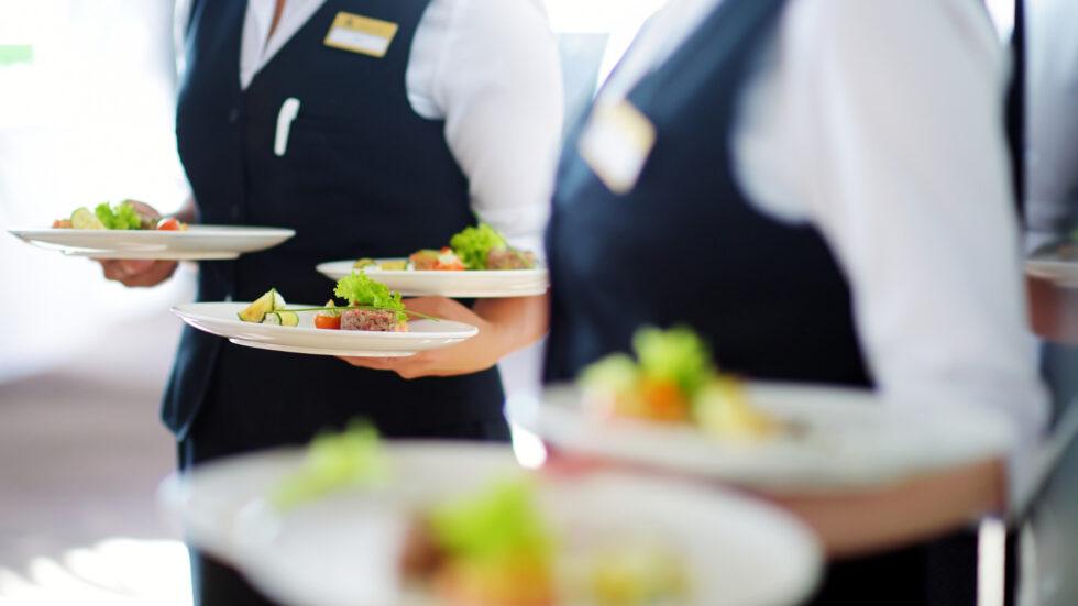 Professional uniformed catering staff carrying multiple elegantly plated dishes to guests at a formal corporate or private dining event