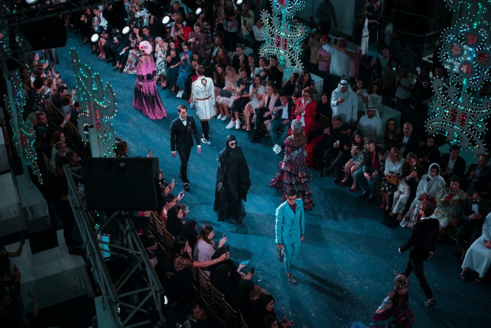 Models walking a glamorous fashion show runway surrounded by an engaged audience at a large-scale event