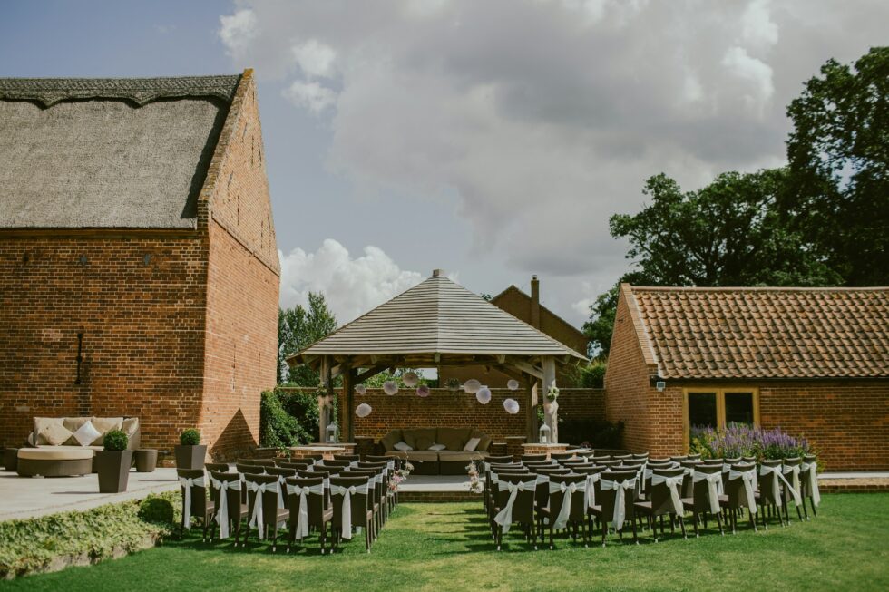 Elegantly decorated outdoor wedding ceremony setup with white ribbon chairs and a gazebo at a professionally staffed private venue