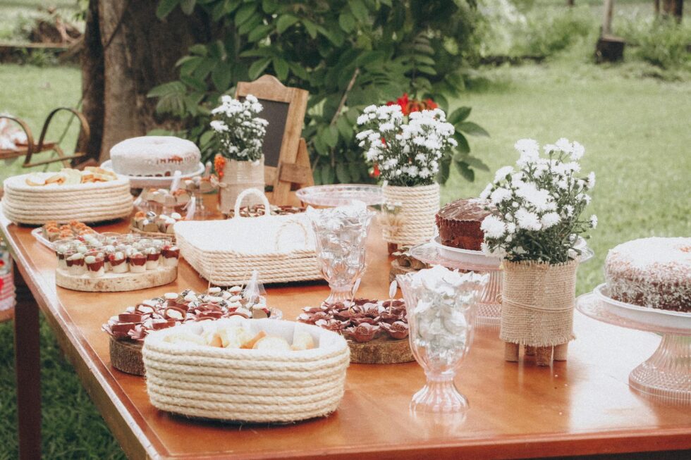 Elegantly styled rustic outdoor dessert table with cakes, sweets, and floral arrangements at a professionally catered private event