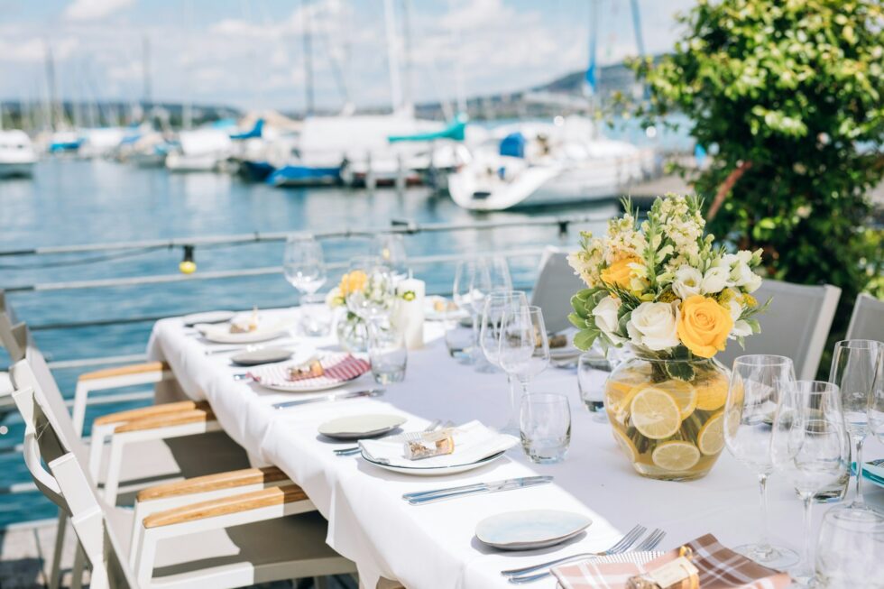 Elegantly set outdoor waterfront dining table with floral centerpiece and fine glassware for a professionally catered private event