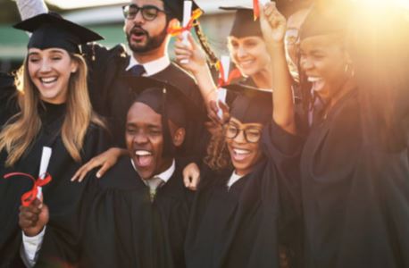 A diverse group of joyful graduates in black caps and gowns celebrating outdoors, laughing and cheering with diplomas in hand, bathed in warm golden sunlight.