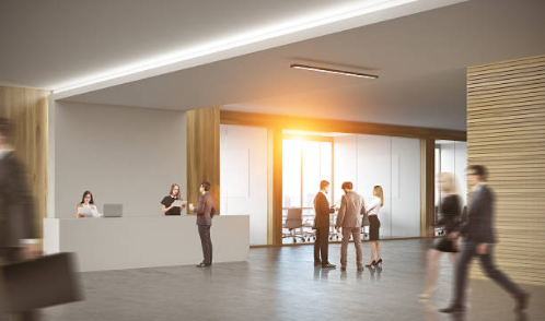 A modern corporate office lobby with a reception desk, warm wood paneling, and floor-to-ceiling windows bathed in golden light, with several professionals conversing and moving through the space.