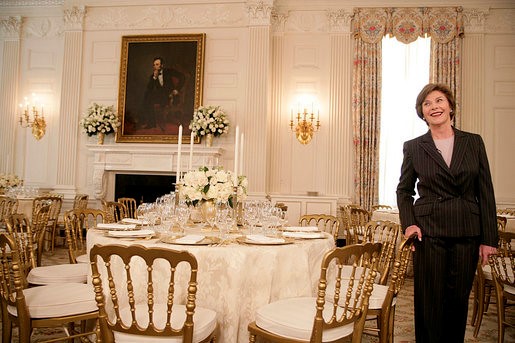 A woman in a dark pinstripe suit smiles while standing in an elegantly appointed formal dining room